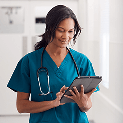 a woman in scrubs with a stethescope reviewing a tablet screen