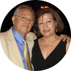 a man with his arm around a woman, both in formal wear and smiling